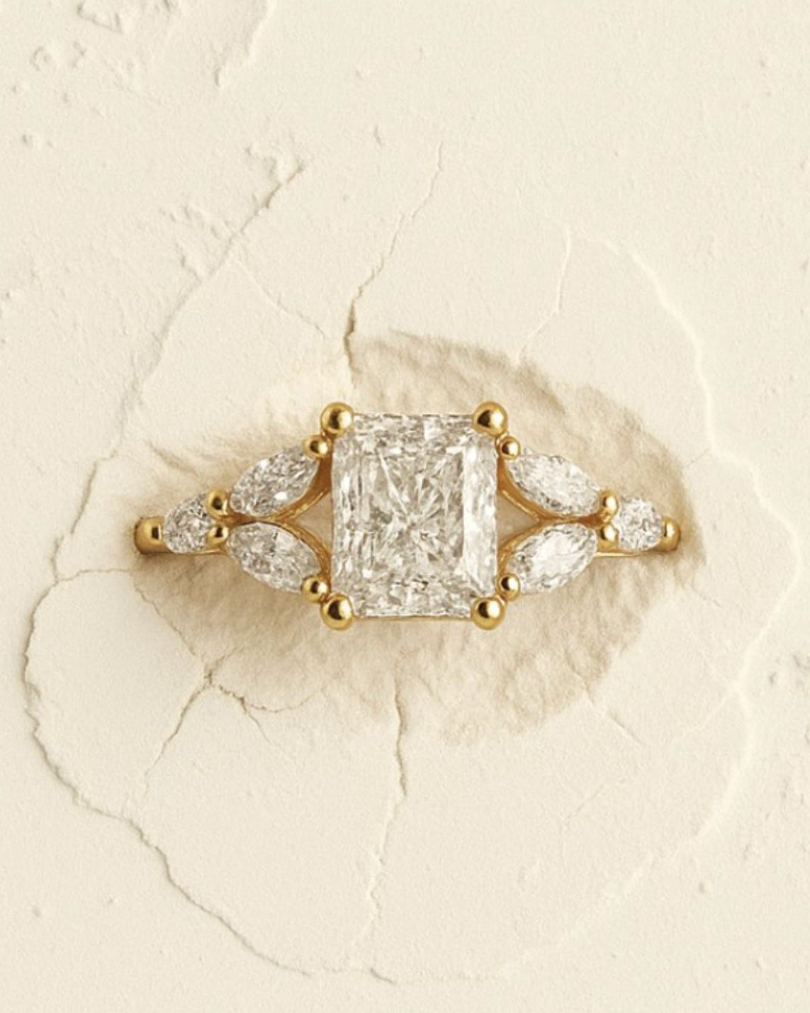 Gold ring with a large diamond and smaller stones on a textured beige background