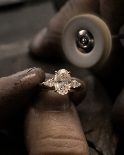 Diamond ring held between fingers with a magnifying glass in the background
