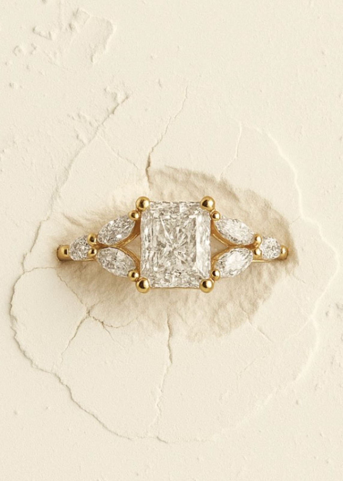 Gold ring with a large diamond and smaller stones on a textured beige background